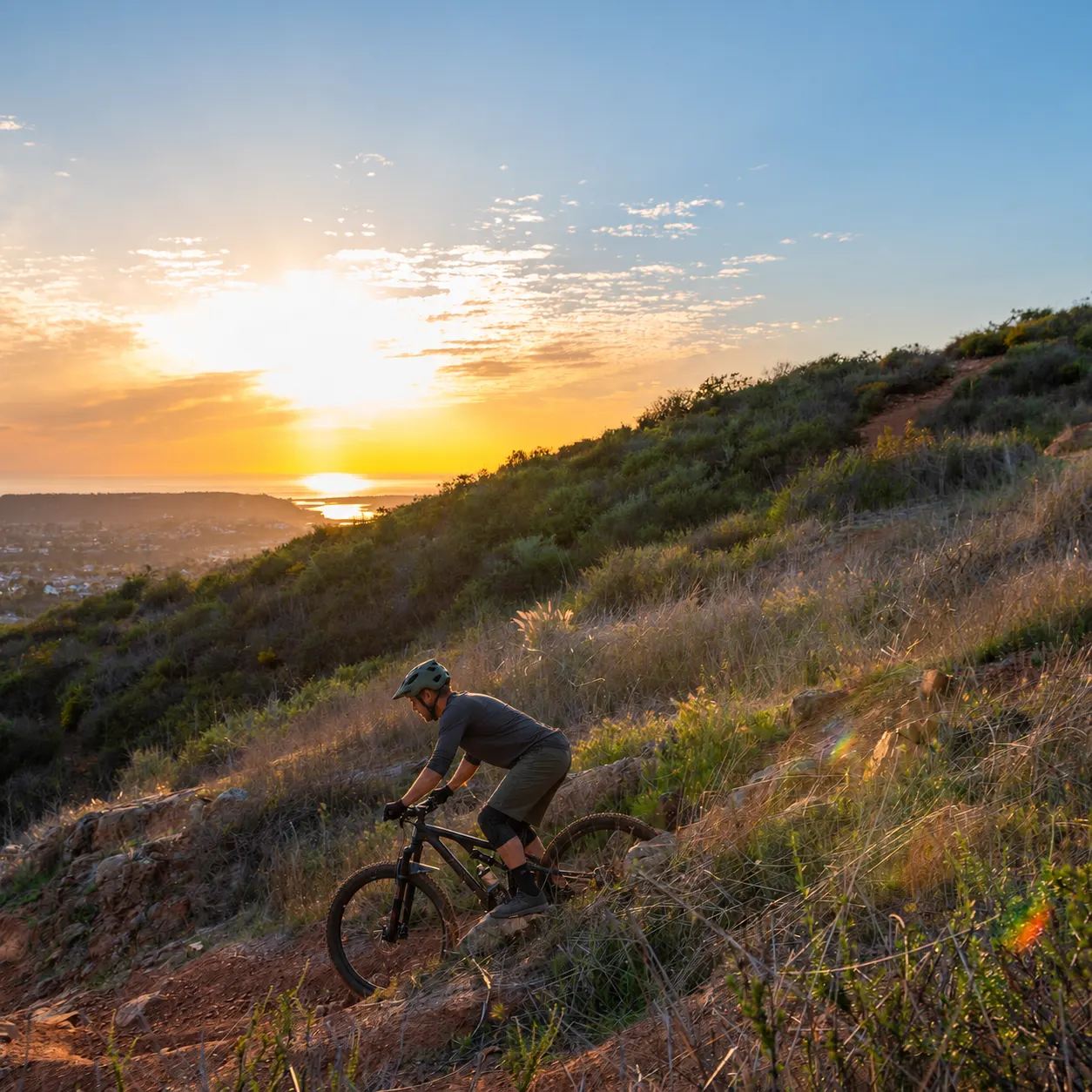 Mountain biker climbing a coastal hillside trail at sunset